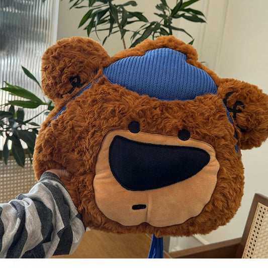 Brown teddy bear-shaped pillow with blue headband on a person indoors.