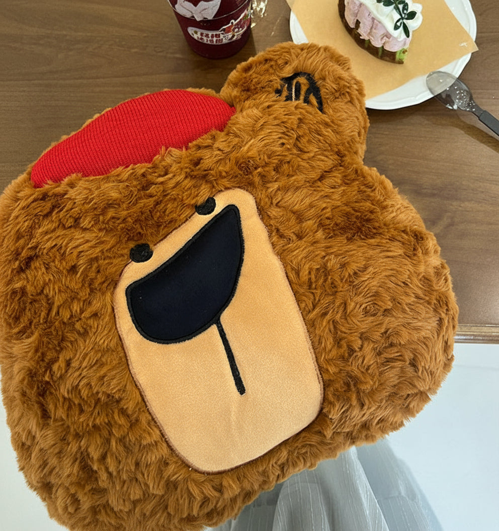 Brown plush toy resembling a bear with a red heart on a wooden table.