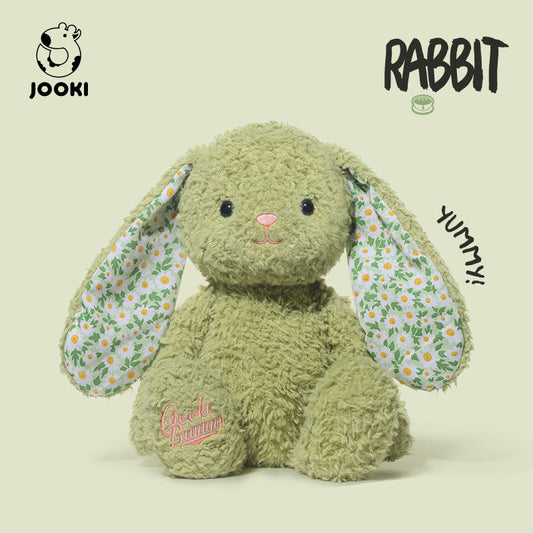 Green plush rabbit toy with floral ears on a beige background, featuring the brand 'Jooki'.