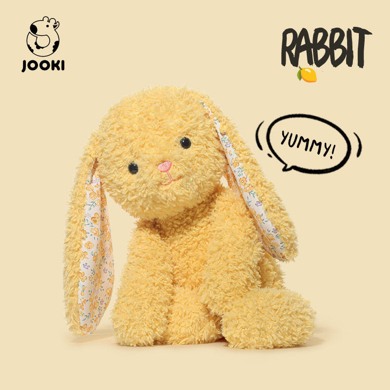 Plush rabbit toy with a speech bubble saying 'YUMMY!' on a beige background, featuring the brand 'Jooki'.