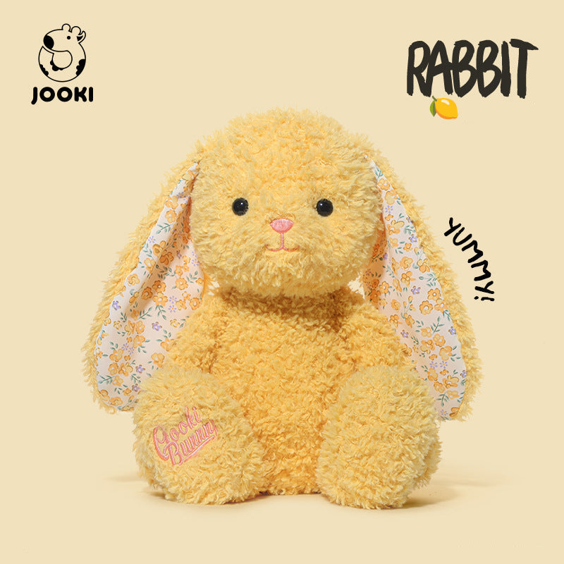 Yellow plush rabbit toy with floral ears on a beige background, featuring the brand 'Jooki'.