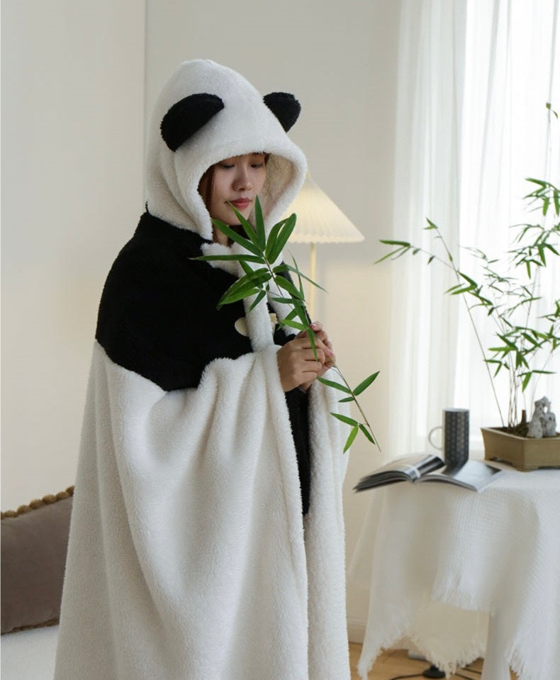 Person wearing a panda-themed blanket in a room with plants and a lamp.