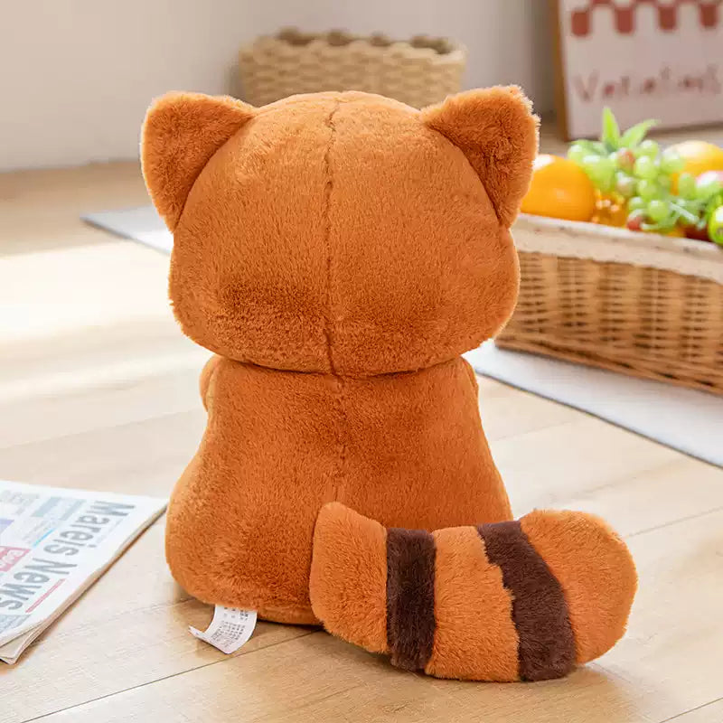 Plush toy shaped like a cat sitting on a wooden floor with a basket of fruits in the background.