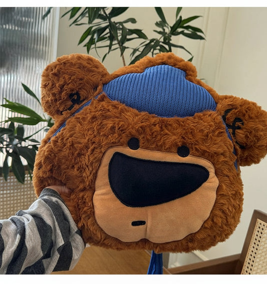 Brown teddy bear-shaped pillow with blue headband on a person indoors.