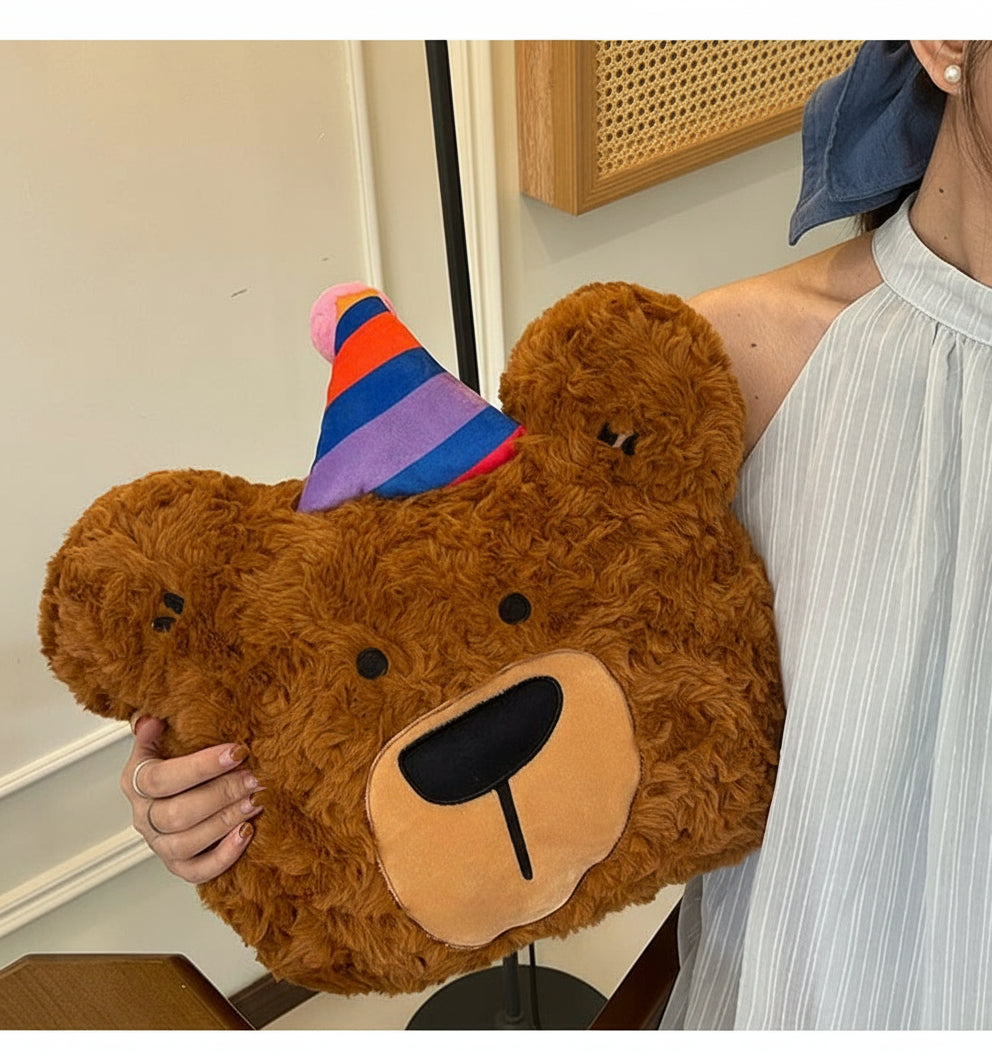 Person holding a large brown teddy bear with a colorful hat indoors.