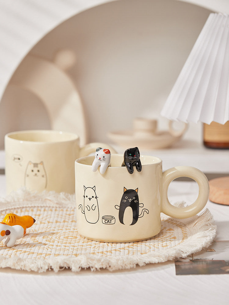 White mug with cat illustrations and cat-shaped cookie cutters on a woven mat.