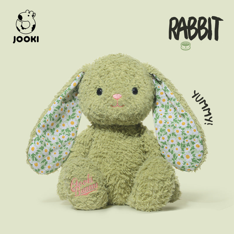 Green plush rabbit toy with floral ears on a beige background, featuring the brand 'Jooki'.