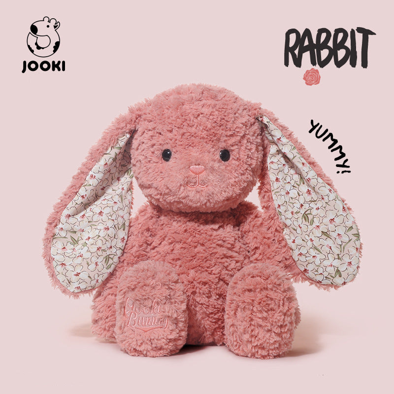 Pink plush rabbit toy with floral ears on a light pink background, featuring the brand 'Jooki'.